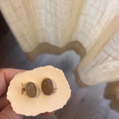Brincos ovalados em metal dourado com pedras castanhas numa base de papel creme
