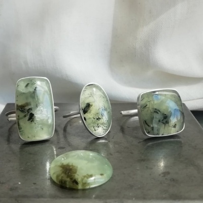 anéis com pedras verdes translúcidas e pedra solta sobre superfície metálica