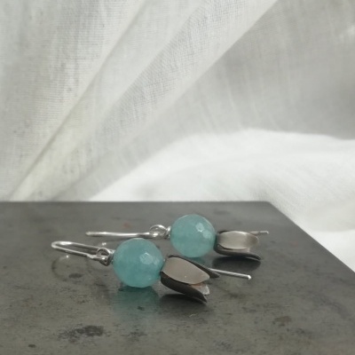 brincos azul-petróleo e prateados sobre superfície cinzenta com fundo branco