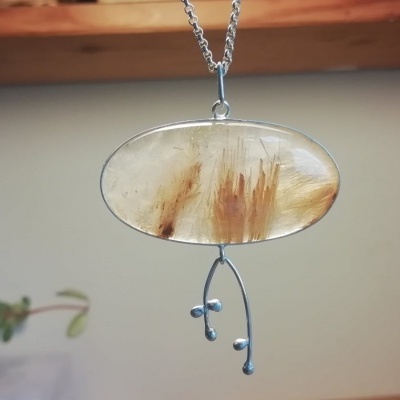 Colar pendente com pedra oval translúcida e detalhes metálicos em forma de ramo