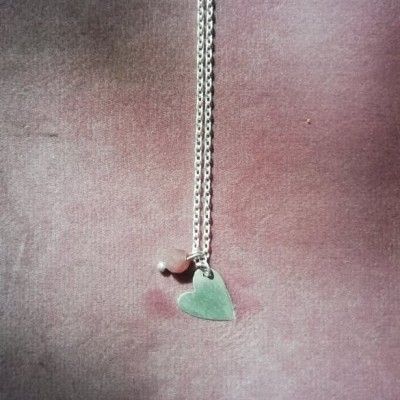 Colar prateado com pendente coração e pérola sobre tecido rosa