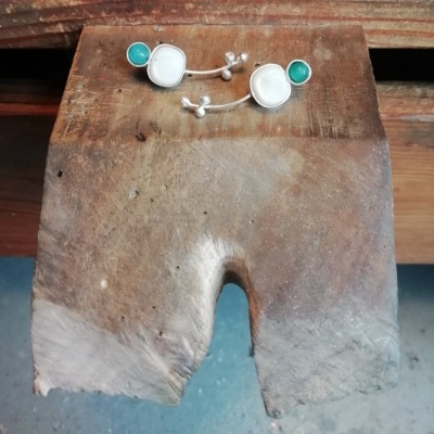 Brincos de prata com pedras branca e verde sobre madeira rústica