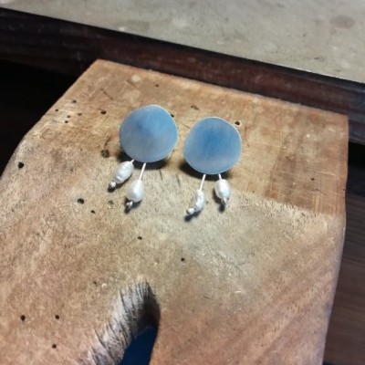 Brincos redondos azulados foscos com pérolas brancas penduradas sobre madeira