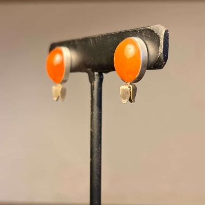 Brincos com pedra oval laranja e metal prateado num suporte negro