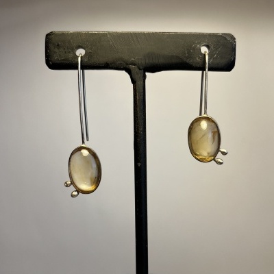Brincos pendentes com pedras ovais amareladas em suporte preto.