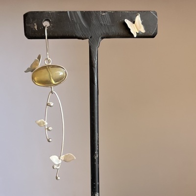 Brinco pendente com pedra amarela e detalhes em folhas e borboletas em suporte preto.