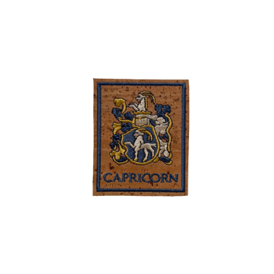 Etiqueta bordada com símbolo do signo Capricórnio em tecido castanho.