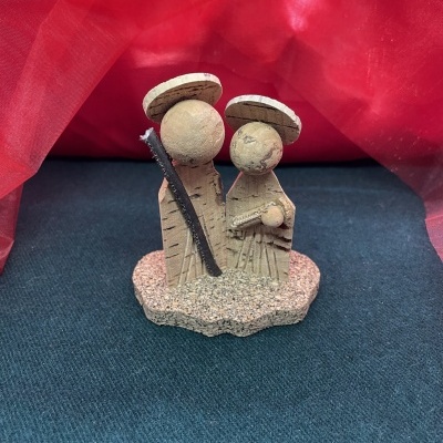 Figuras decorativas de madeira com chapéus redondos sobre tecido azul escuro e fundo vermelho.