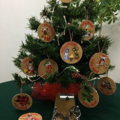 Mini árvore de Natal artificial verde com pendentes circulares de cortiça decorados, em mesa verde.