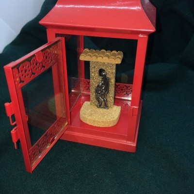 Lanterna metálica vermelha com porta de vidro aberta e figura interior