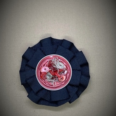 Broche redondo com base preta e centro rosa decorado com contas e fio metálico