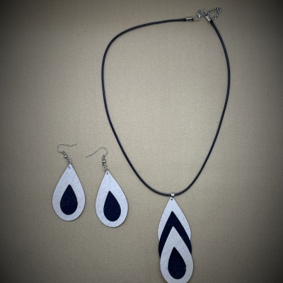 Conjunto de colar e brincos em forma de gota branco e preto, sobre fundo cinzento.