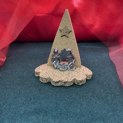 Pequeno presépio de cortiça com figuras metálicas e estrela, sobre fundo preto com pano vermelho atrás