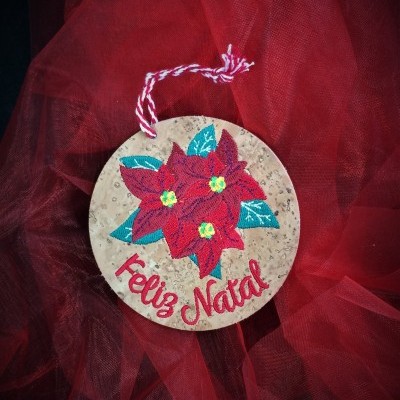 Ornamento redondo de cortiça com flores vermelhas e texto 'Feliz Natal'