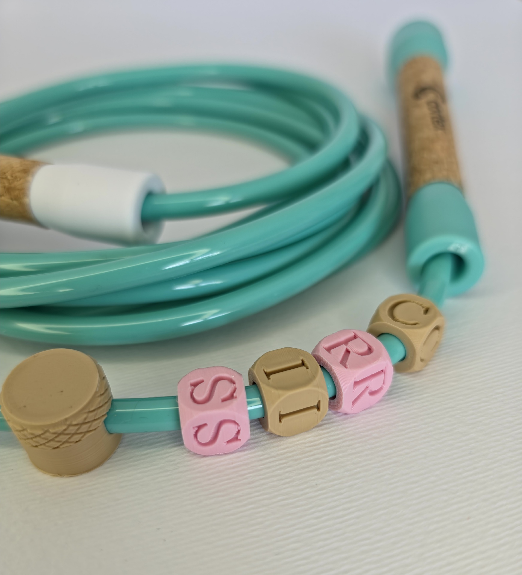 Turquoise skipping rope with cork handles and lettered beads on a white surface