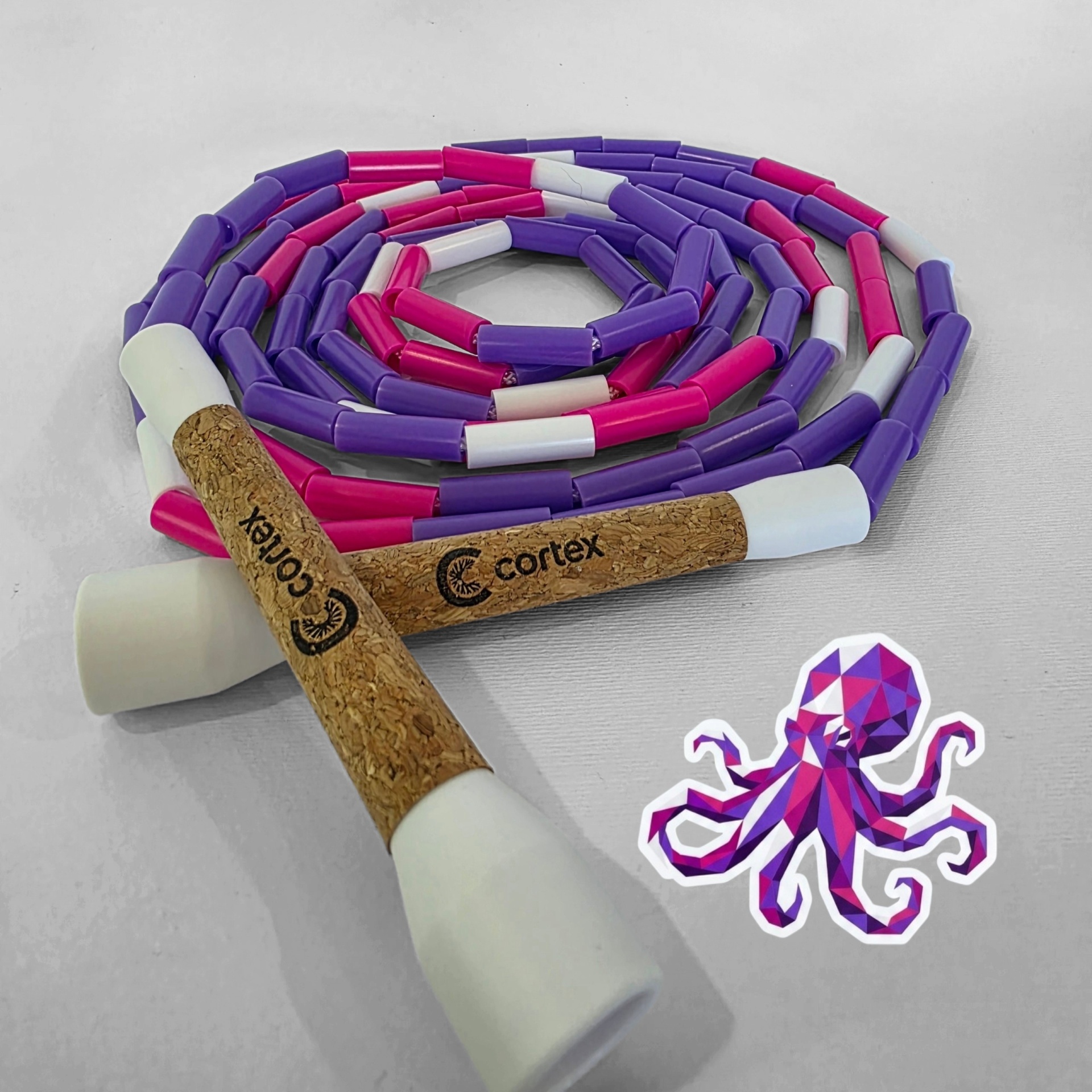 Coiled beaded jump rope with cork handles and a colorful octopus sticker on white surface