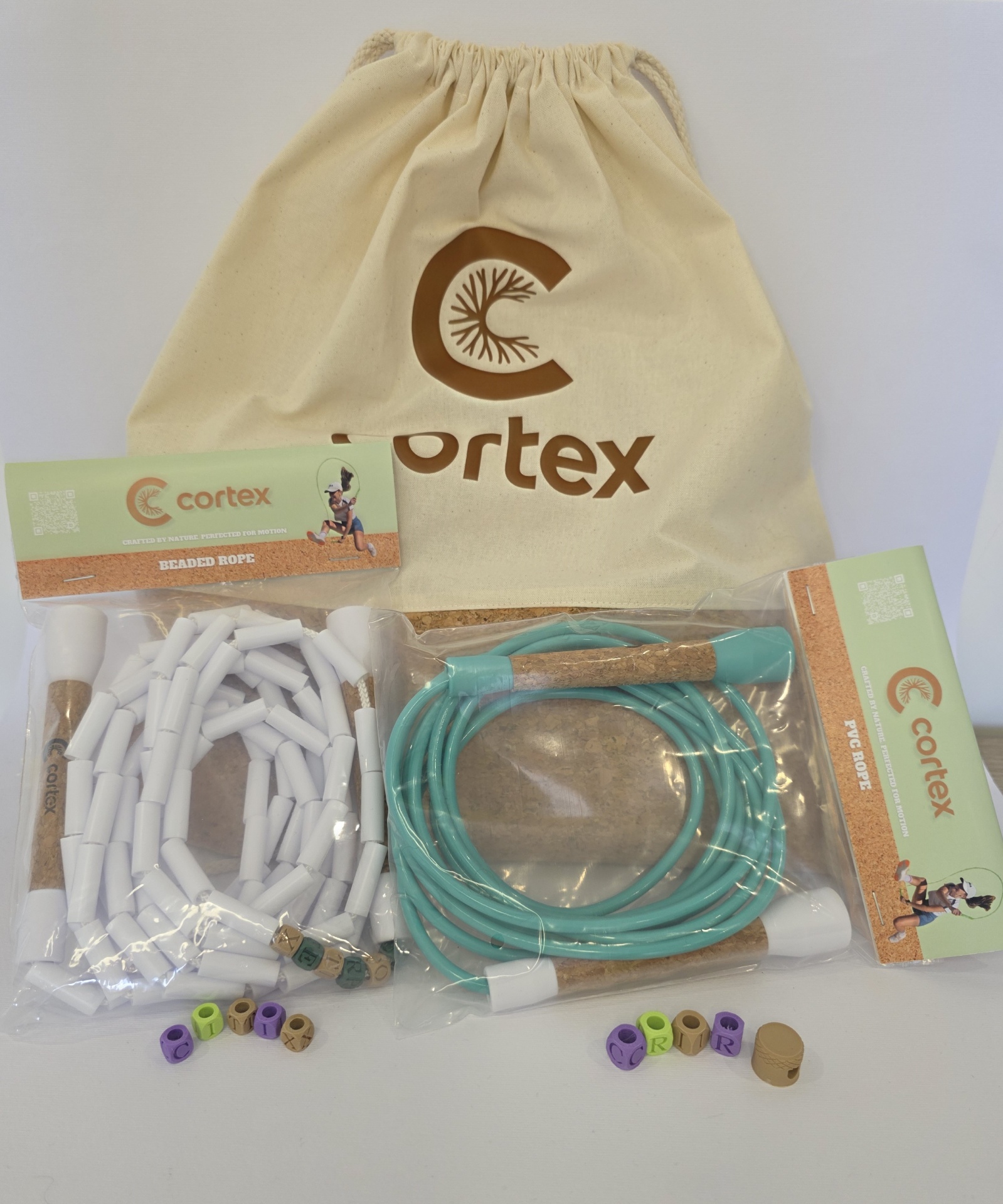Two different skipping ropes with cork handles, beige drawstring bag labeled Cortex, and colored beads spelling CORTEX
