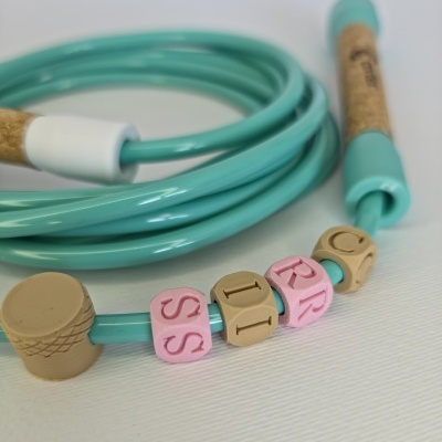 Turquoise skipping rope with cork handles and lettered beads on a white surface