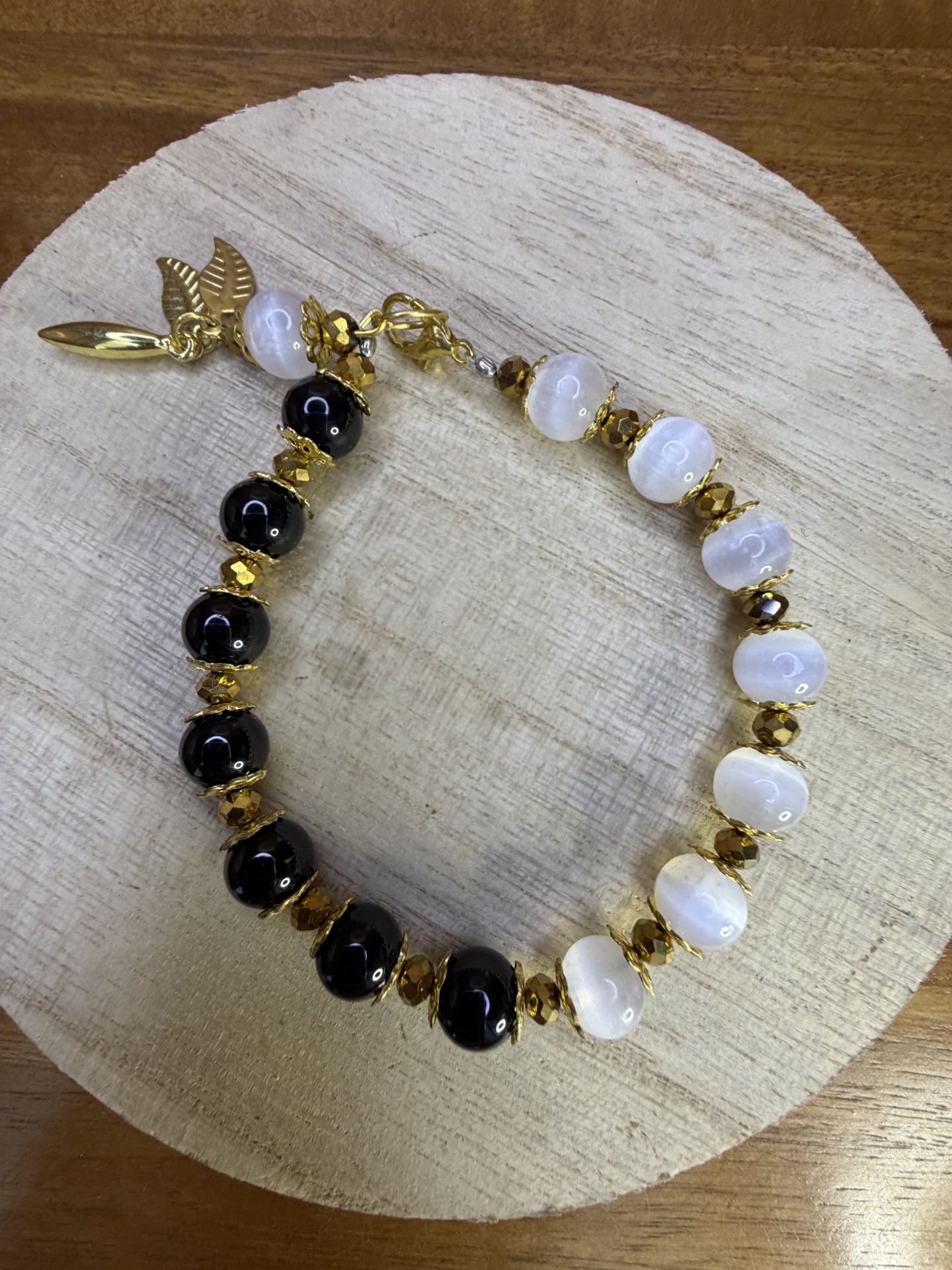 Pulseira com contas pretas e brancas com detalhes dourados sobre madeira clara