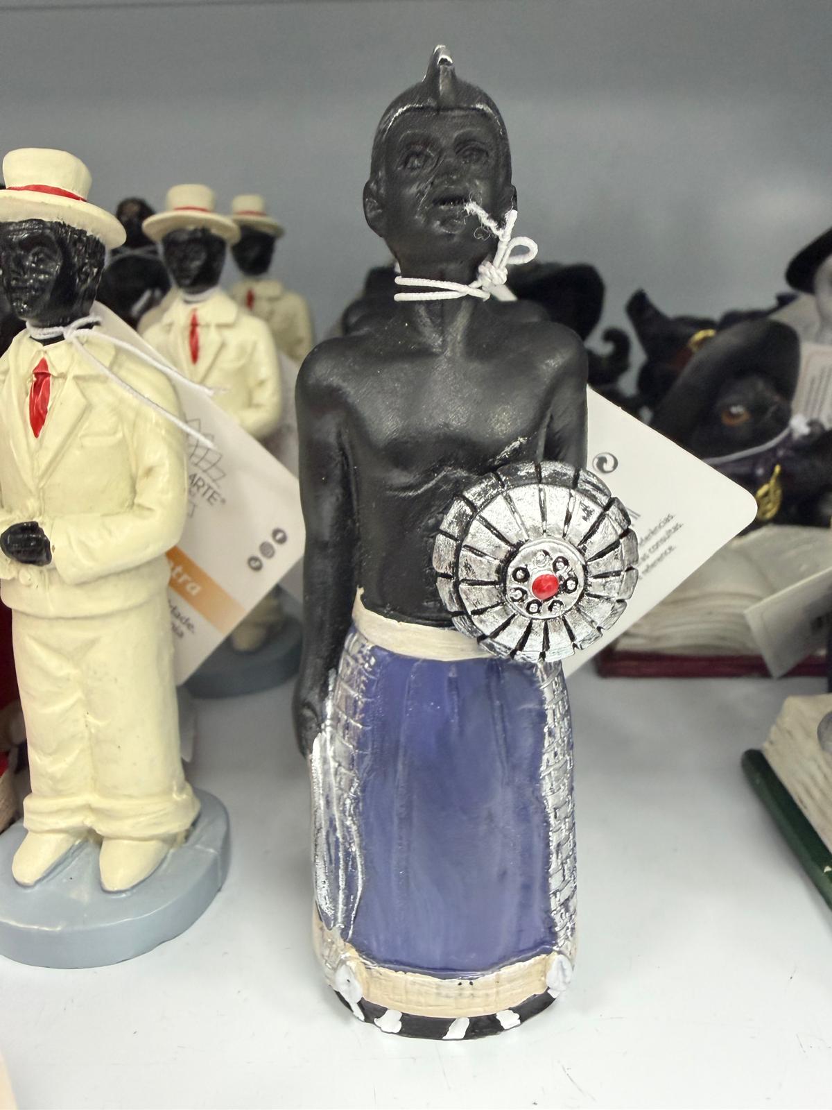 Estátua decorativa de figura humana com saia azul e objeto prateado