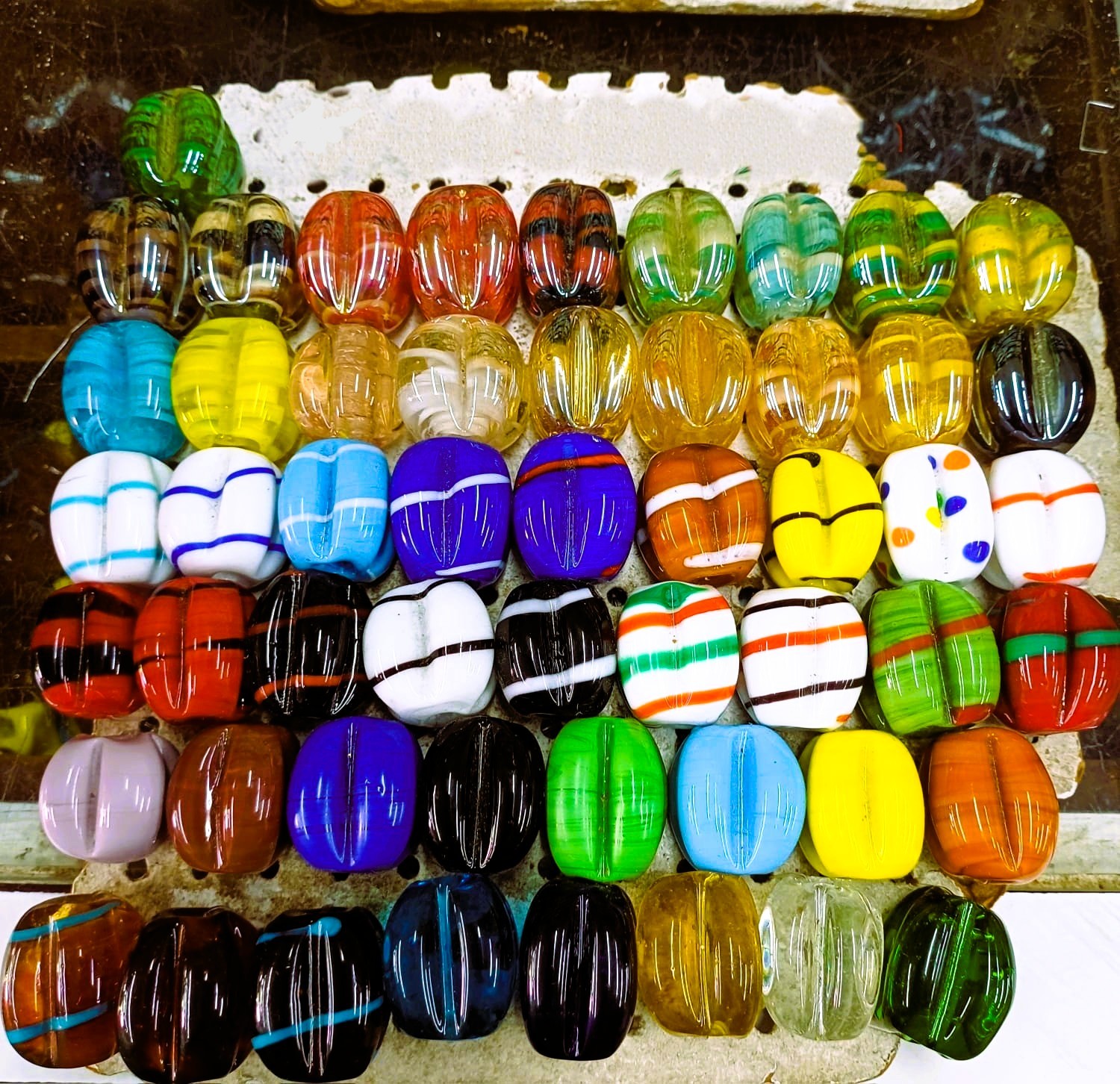 Botões grandes coloridos de vidro com vários padrões e cores, organizados em filas sobre uma superfície rústica.