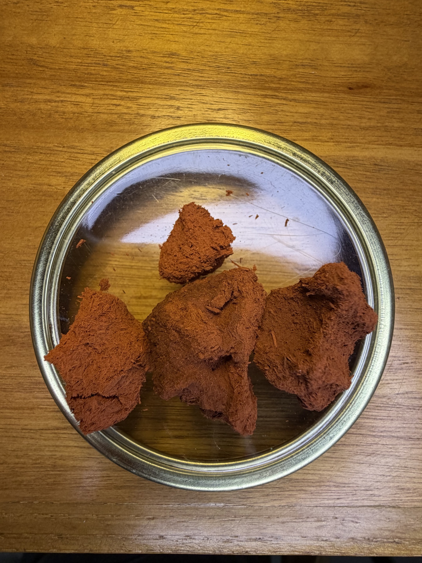 Tigela metálica com pedaços de material marrom avermelhado sobre mesa de madeira