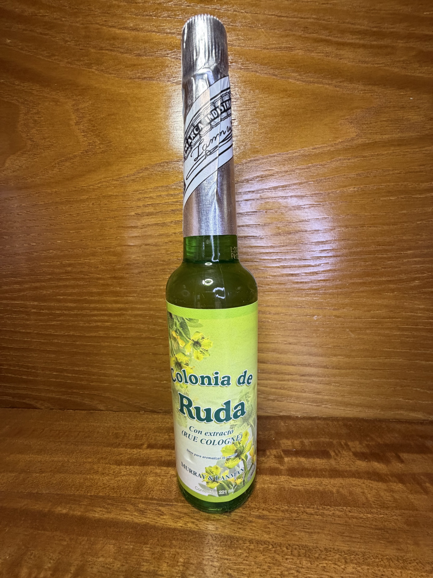 Garrafa verde com rótulo amarelo com flores e texto em cima de superfície de madeira.