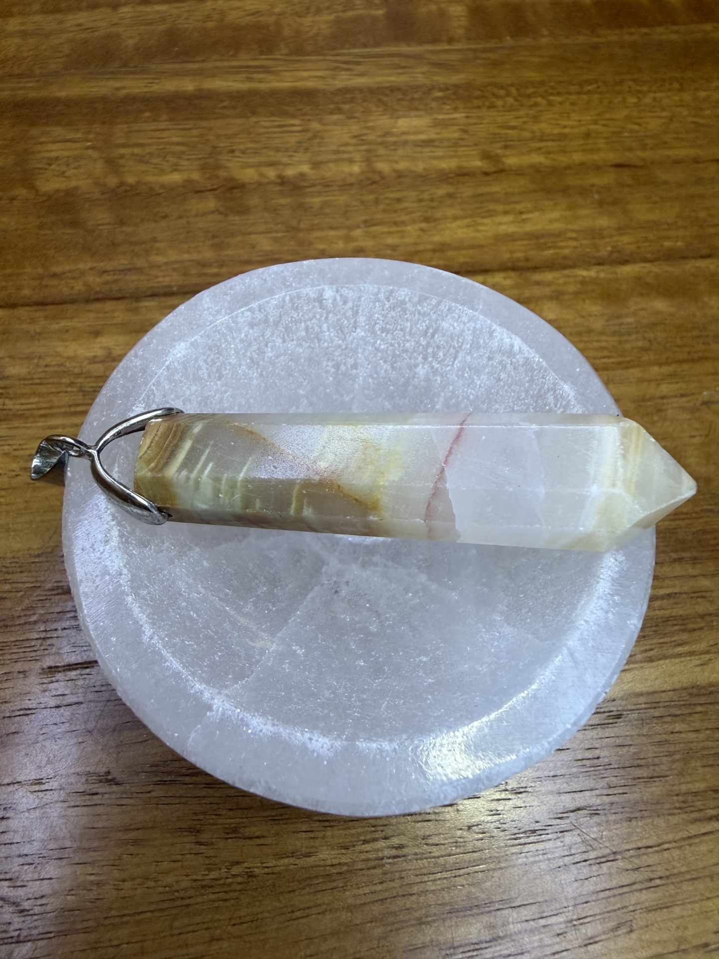 Pingente em pedra multifacetada com suporte metálico sobre base branca circular.