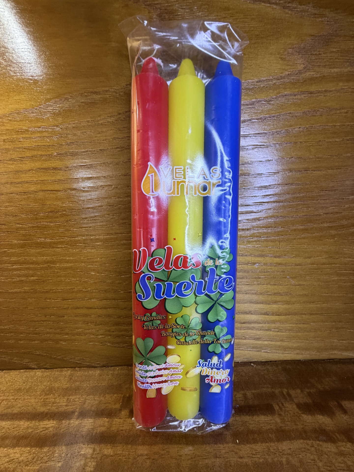 Conjunto de três velas coloridas (vermelha, amarelo e azul) embaladas em plástico transparente com texto visível