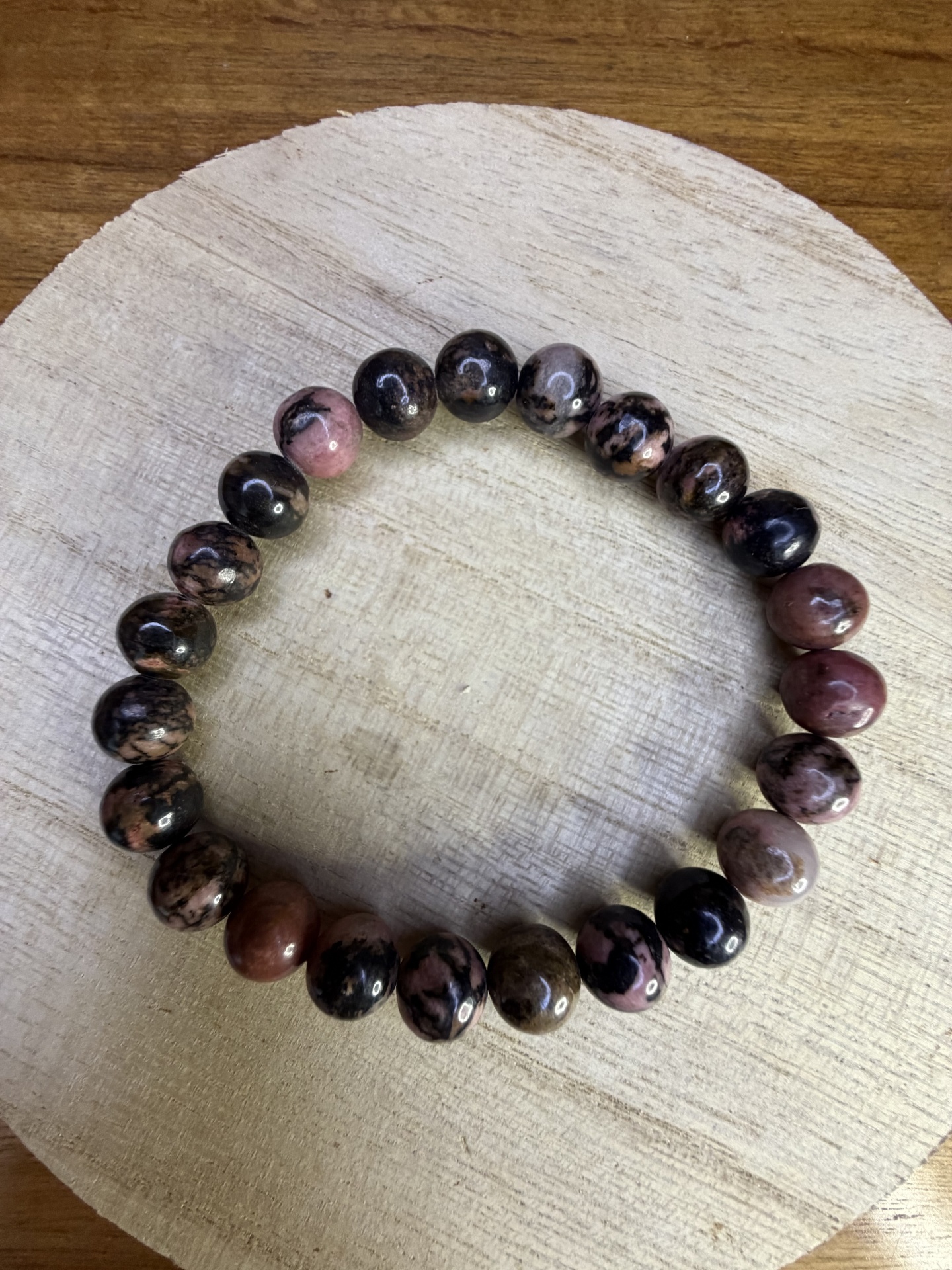 Pulseira com contas rosa e pretas em superfície de madeira clara