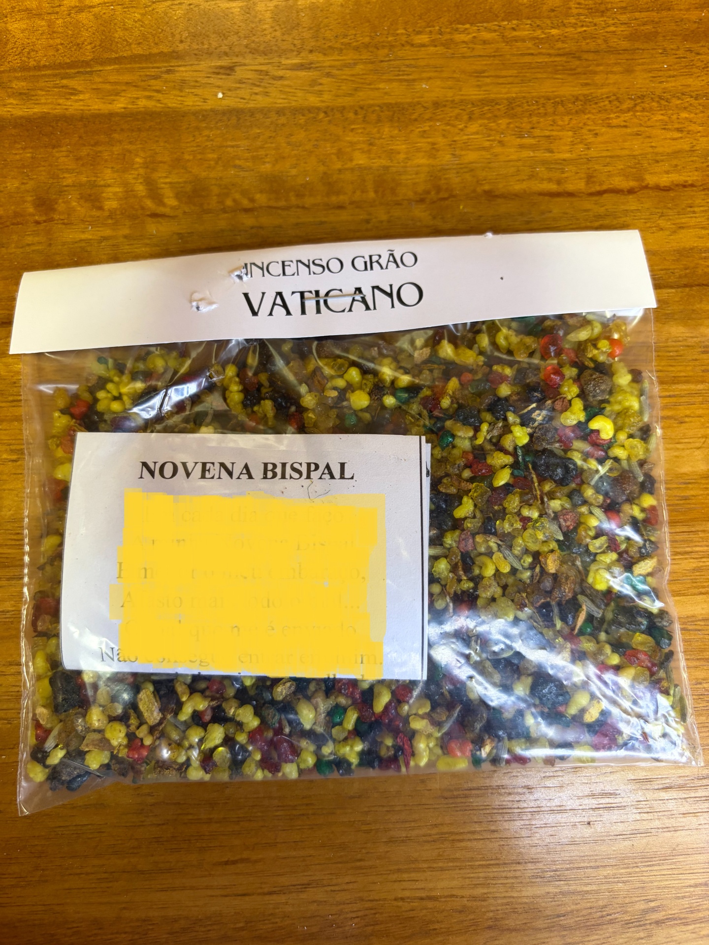 Pacote de resina colorida para incenso com etiquetas VATICANO e NOVENA BISPAL sobre mesa de madeira