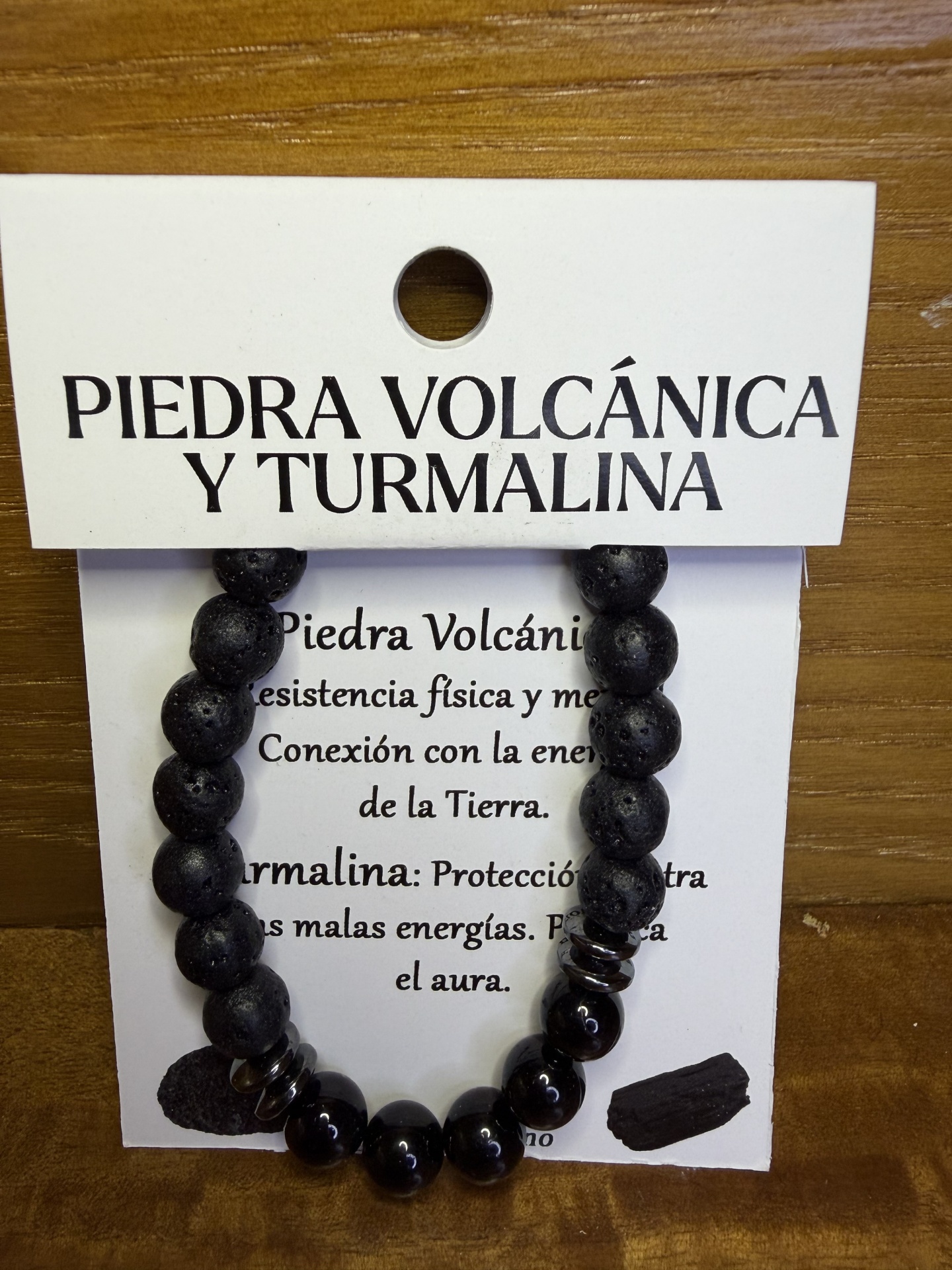 Pulseira com pedras pretas vulcânicas e turmalina num cartão informativo com texto em espanhol