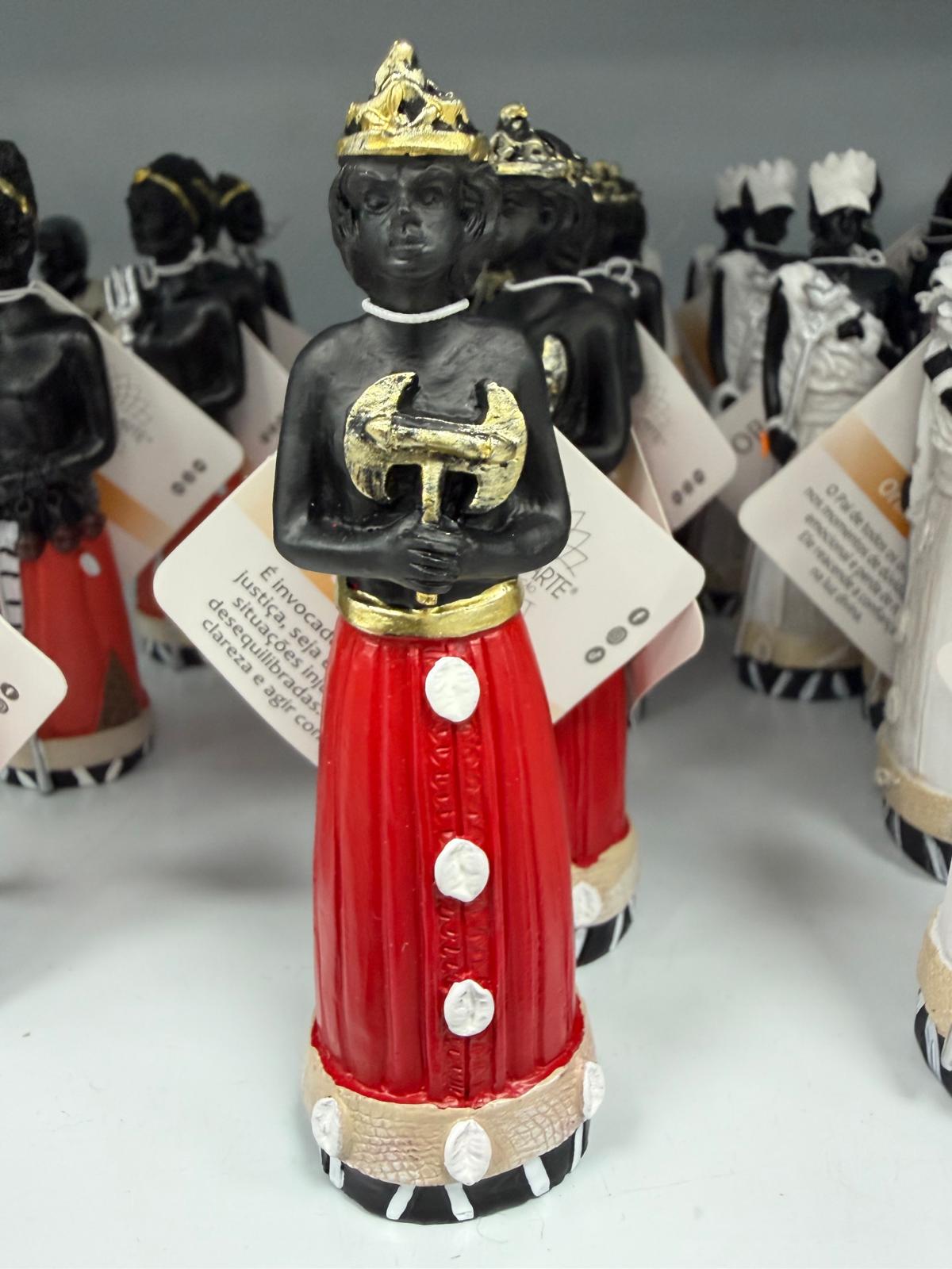 Estatueta de figura com coroa dourada e vestido vermelho com botões brancos.