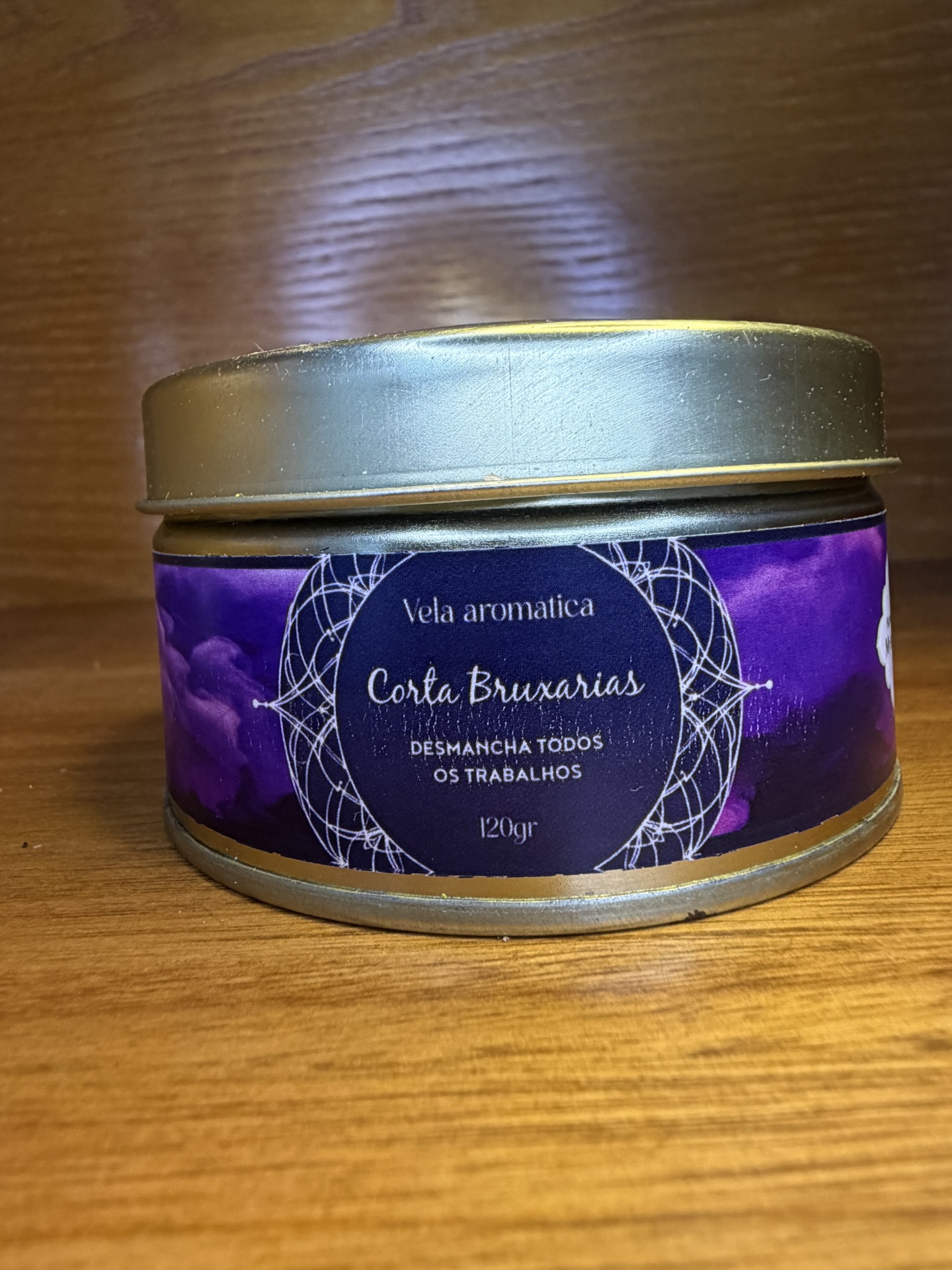 Frasco metálico com rótulo roxo de vela aromática Corta Bruxarias sobre madeira