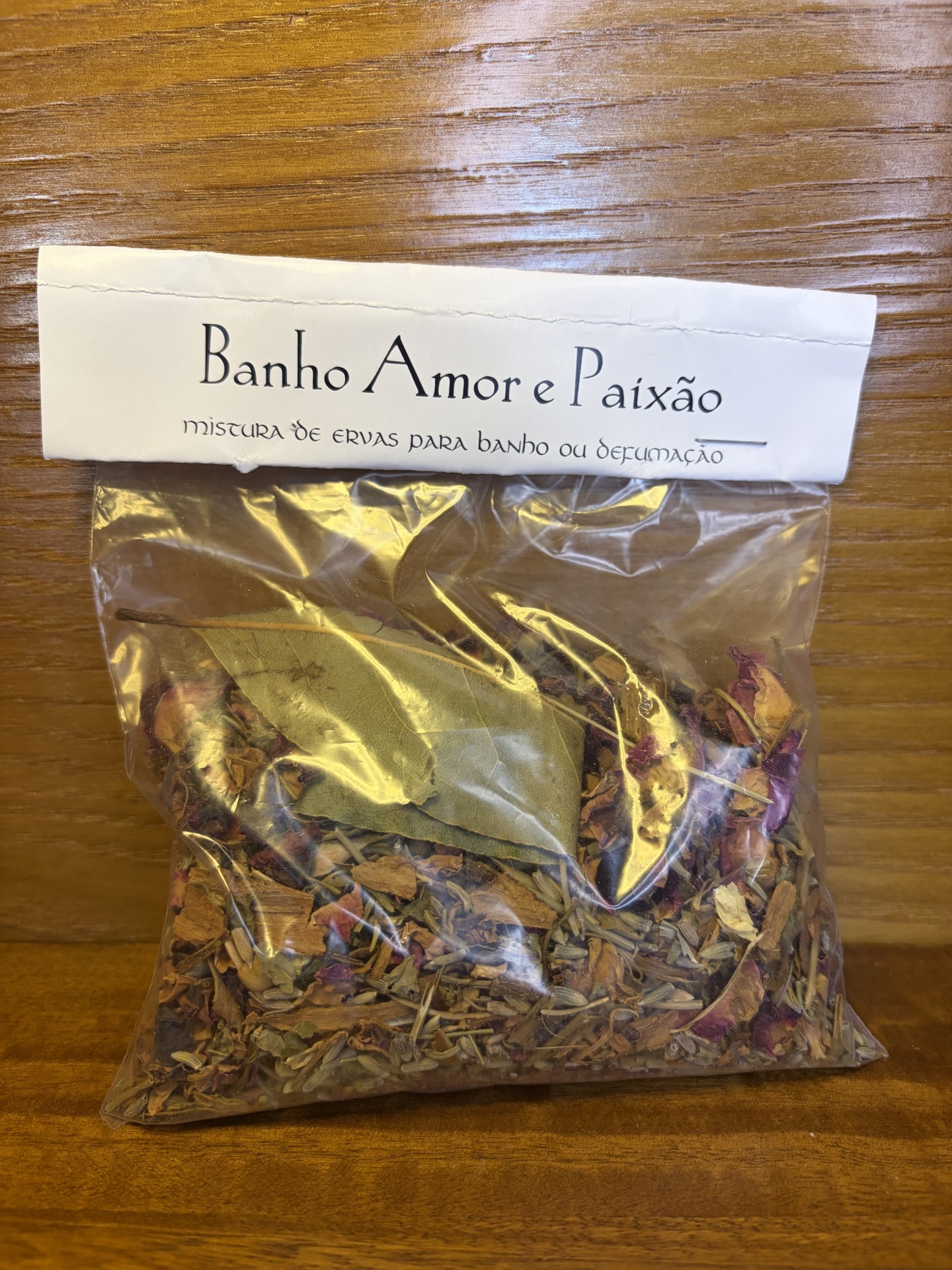 Pacote de ervas secas com etiqueta Banho Amor e Paixão em superfície de madeira.
