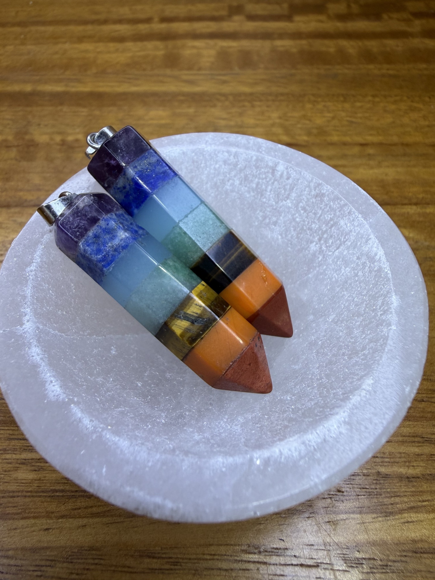 Dois pendentes triangulares multicoloridos dentro de tigela branca sobre mesa de madeira