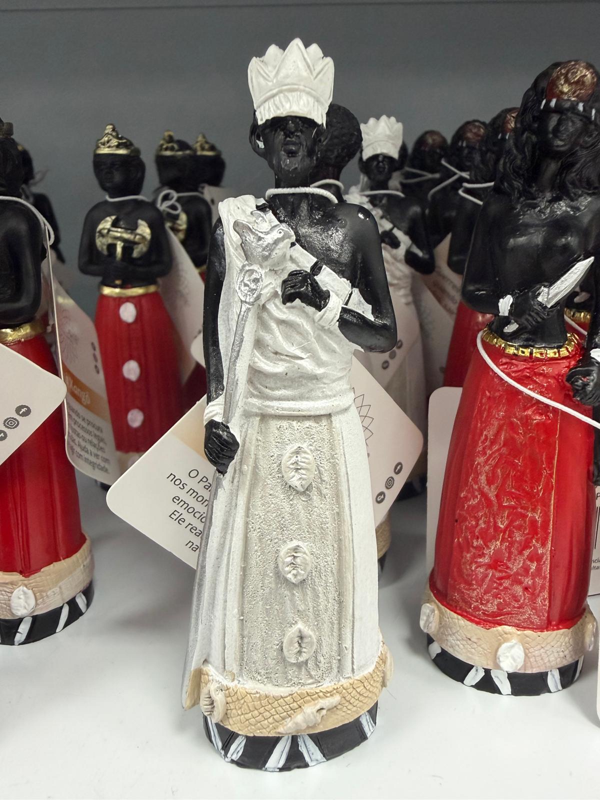 Figuras decorativas de homens negros com roupas brancas e vermelhas e coroas em uma prateleira