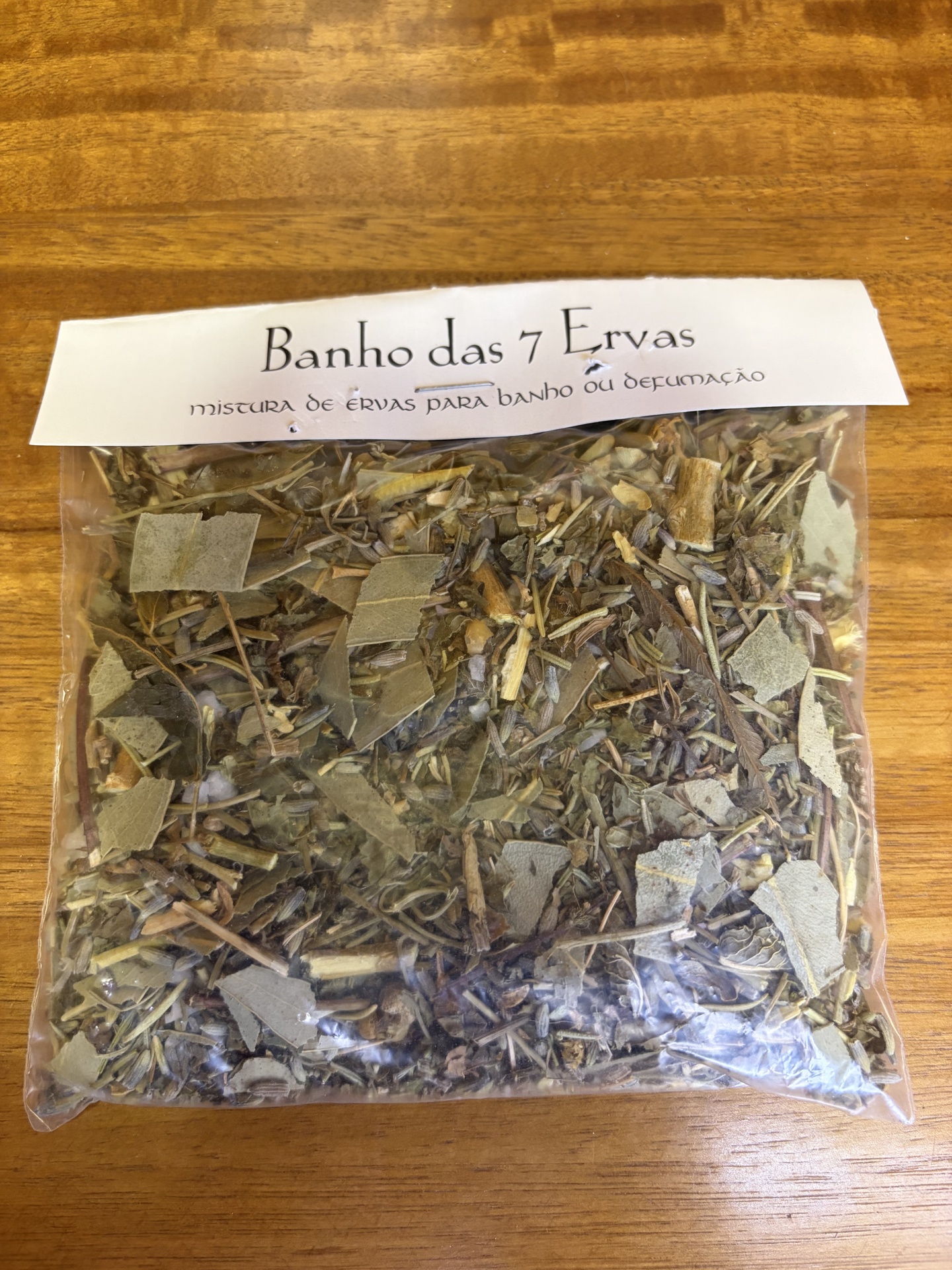 Pacote de ervas secas com etiqueta branca Banho das 7 Ervas sobre mesa de madeira
