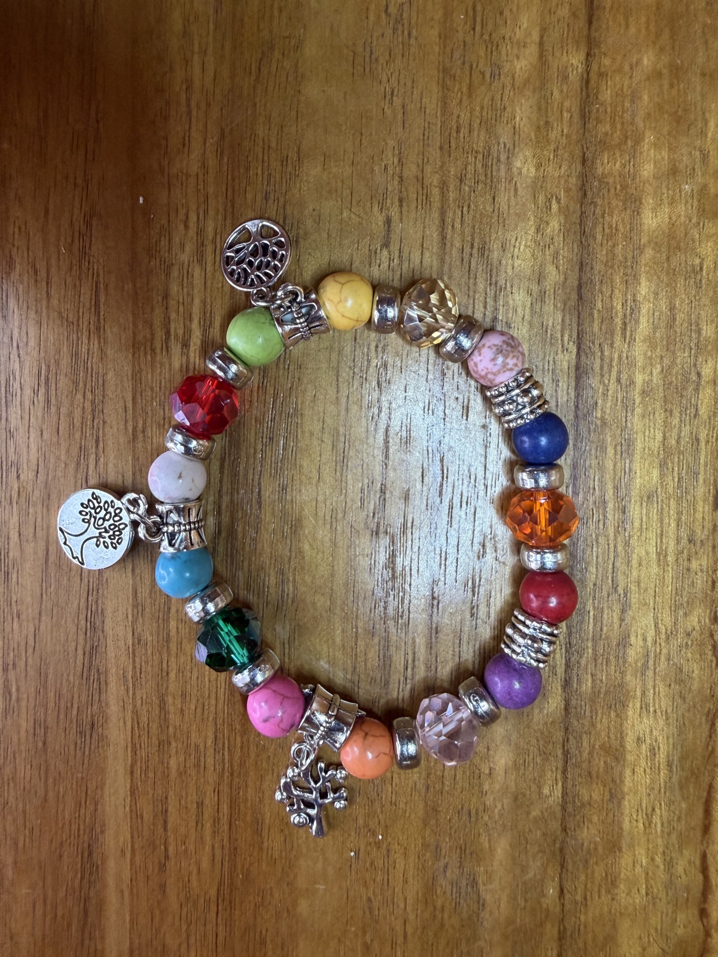 Pulseira colorida com contas e pendentes prateados em fundo de madeira.