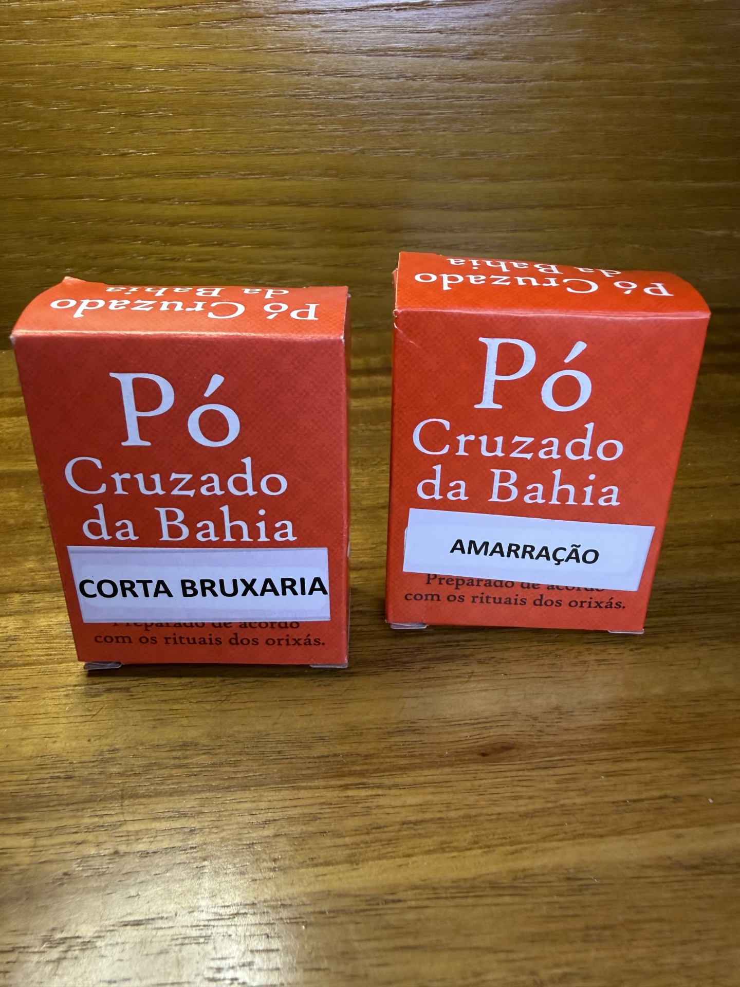 Caixas vermelhas de pó Cruzado da Bahia com etiquetas CORTA BRUXARIA e AMARRAÇÃO
