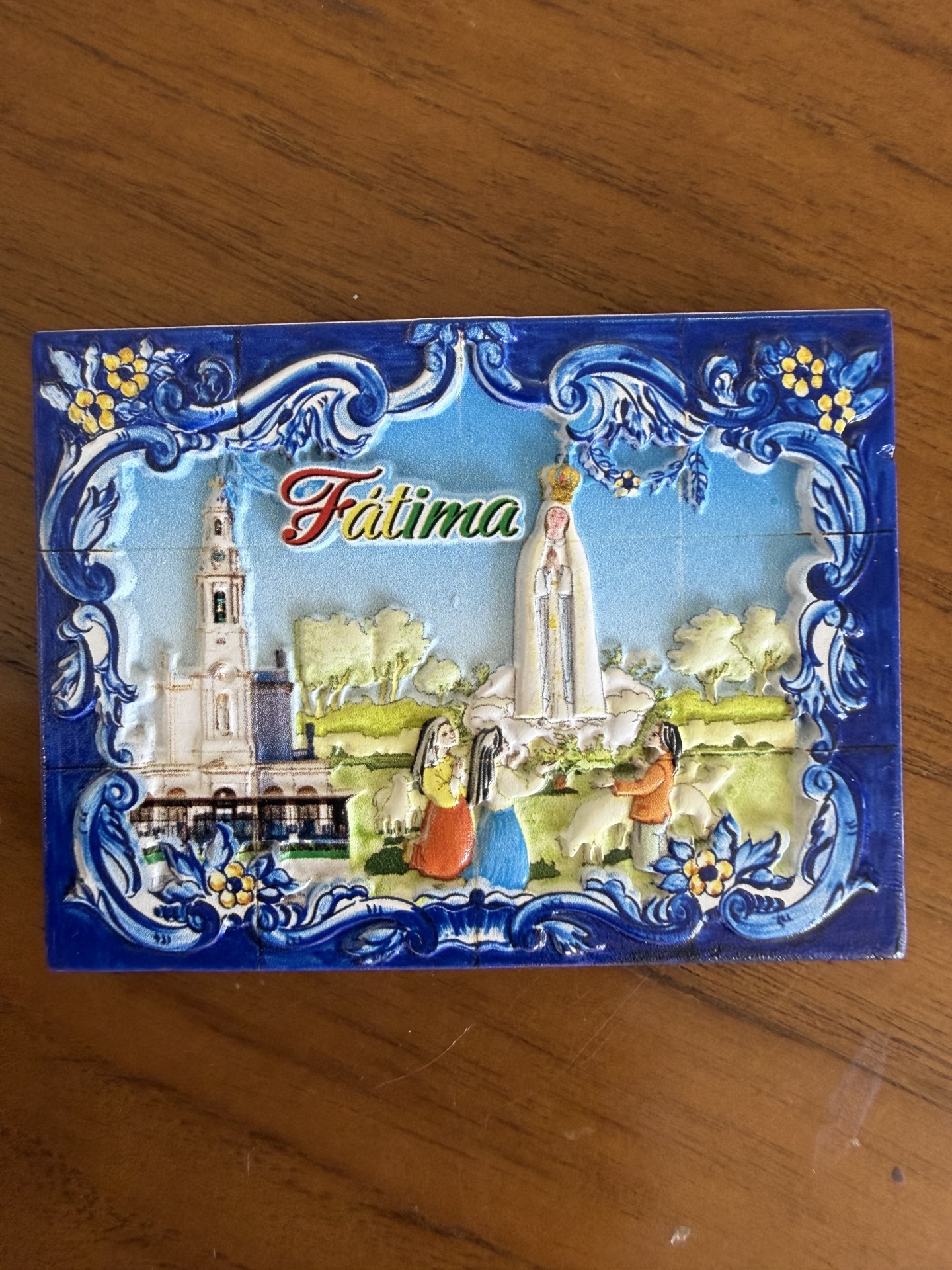 Azulejo decorativo da Basílica de Fátima com moldura azul e figuras humanas em cerâmica