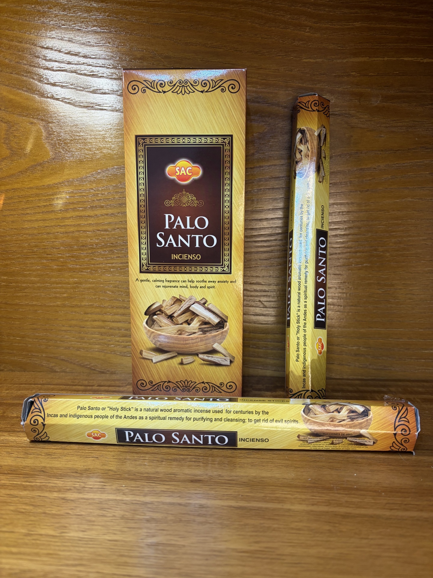 Três embalagens de incenso Palo Santo da marca SAC com decoração dourada e castanha, e imagem de madeira e pedaços de Palo Santo.