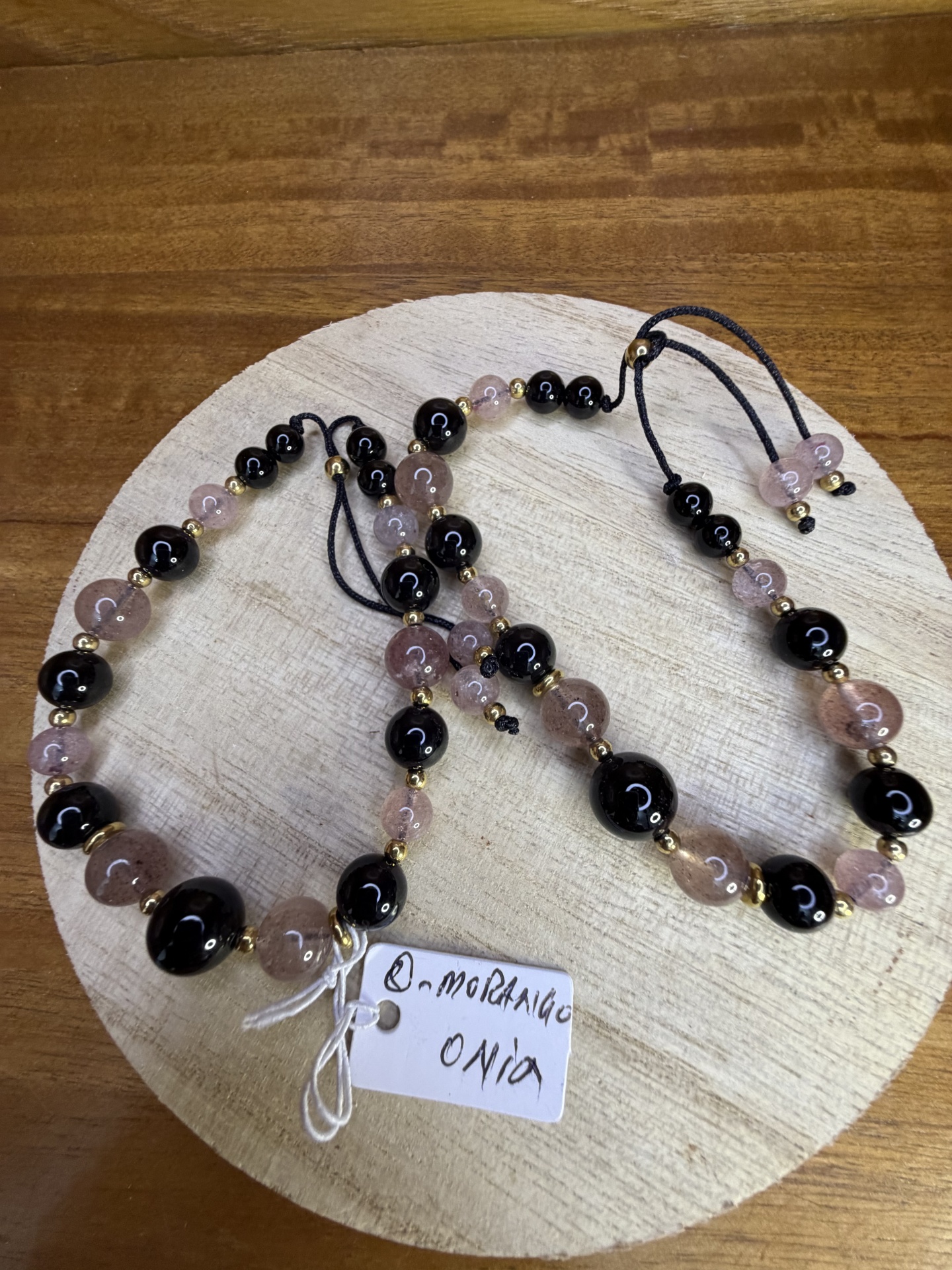 Colar e pulseira com contas cor-de-rosa translúcido, preto e dourado sobre base de madeira clara