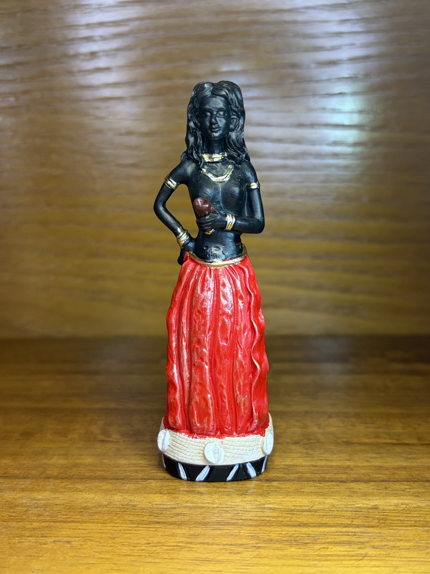 Estátua de mulher com saia vermelha sobre superfície de madeira clara