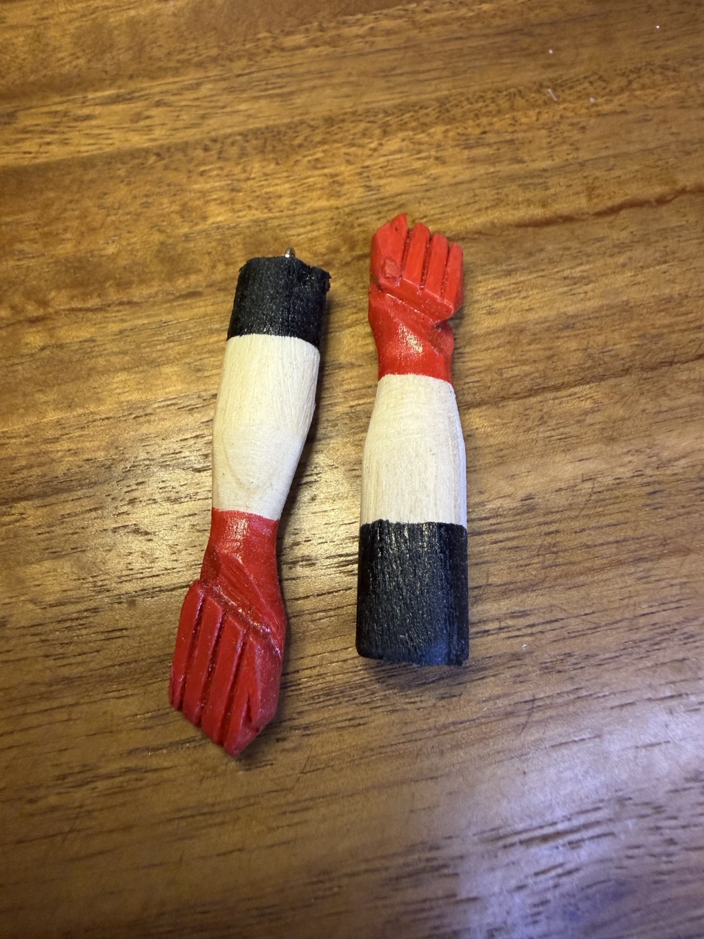 Pendurantes em forma de braços de madeira pintada em vermelho, branco e preto.