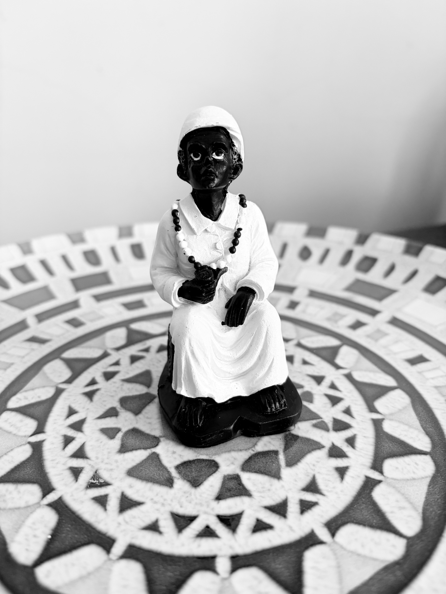 Estátua pequena com figura negra vestindo branco, sobre mesa com padrão geométrico.