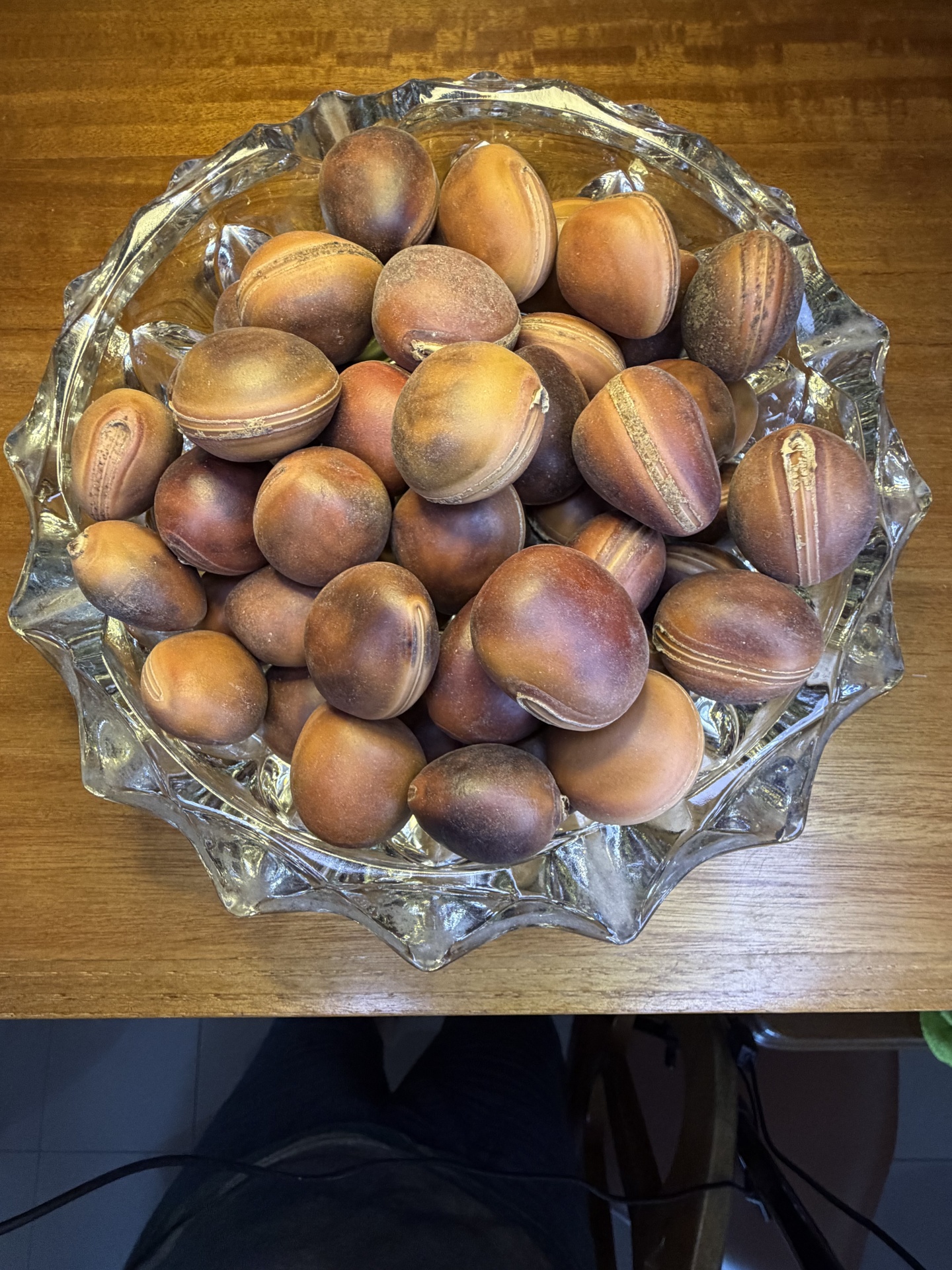 Taça de vidro com castanhas em casca sobre mesa de madeira
