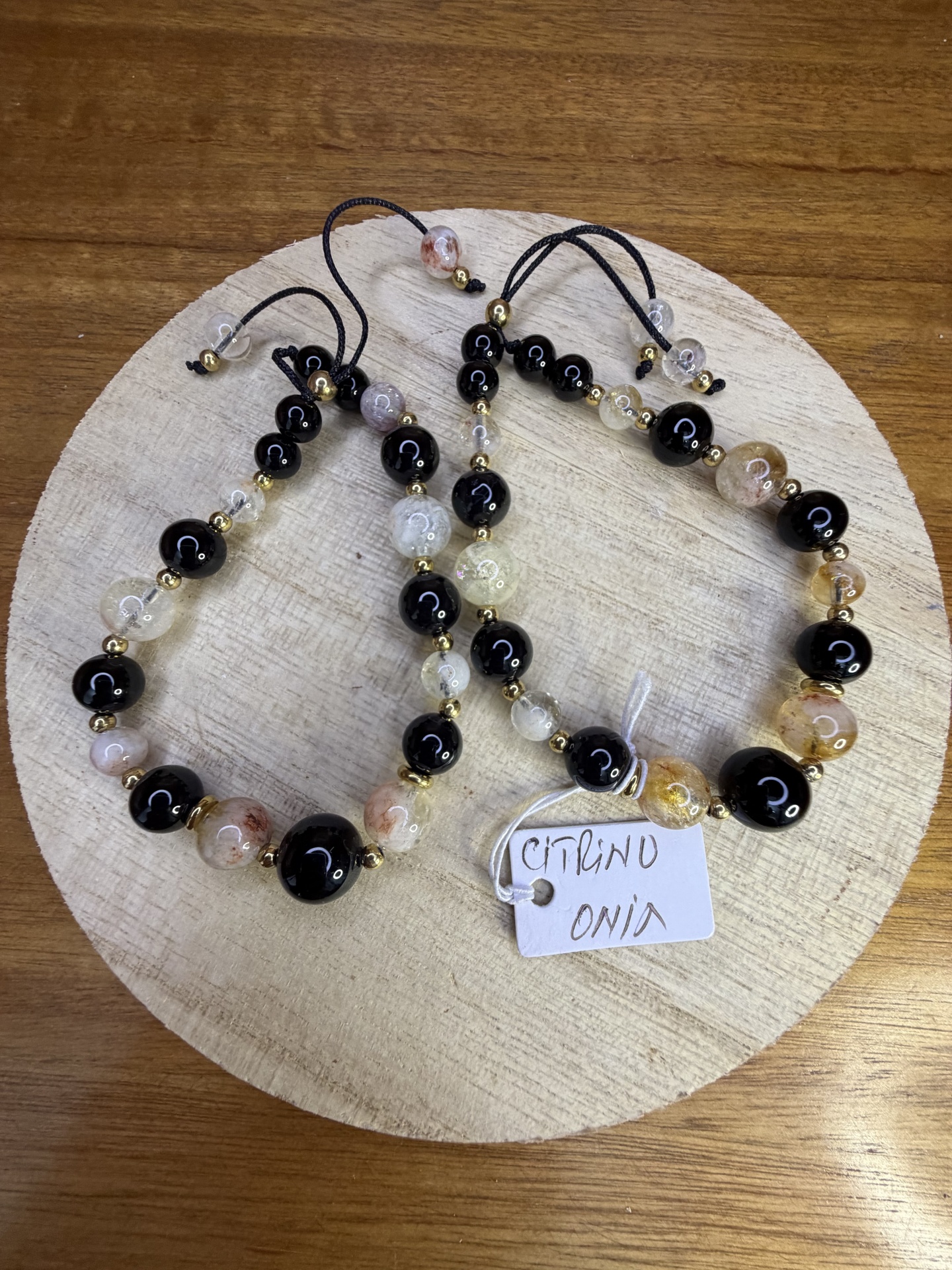 Pulseiras de contas pretas, Âmbar e transparentes com pequenas contas douradas sobre base de madeira clara