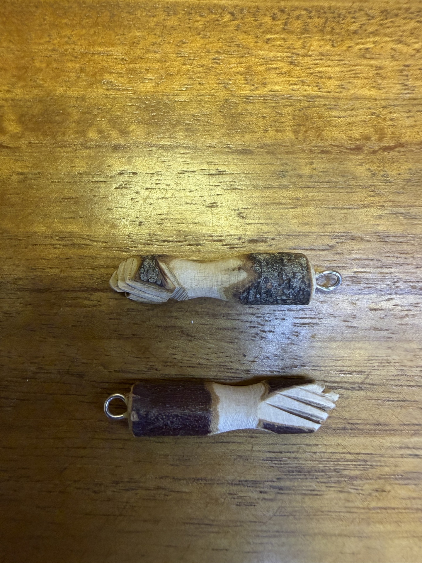 Dois amuletos em madeira com argola metálica sobre madeira clara