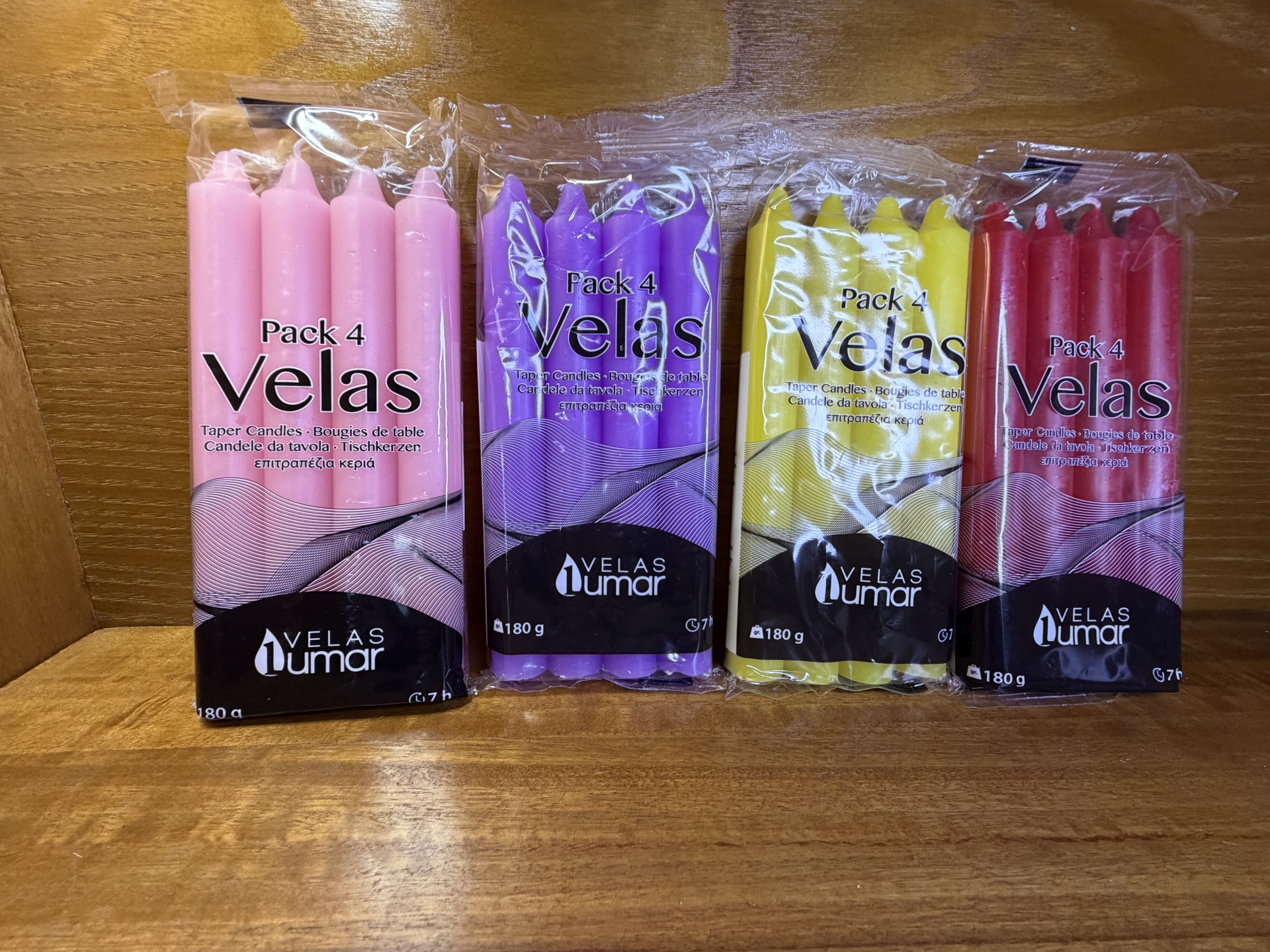 Pacotes de velas cónicas em plástico transparente, 4 unidades por embalagem, cores rosa, roxa, amarela e vermelha.